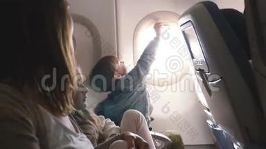 快乐好奇的小男孩在飞行中打开飞机窗盖，享受与家人一起度假的风景。